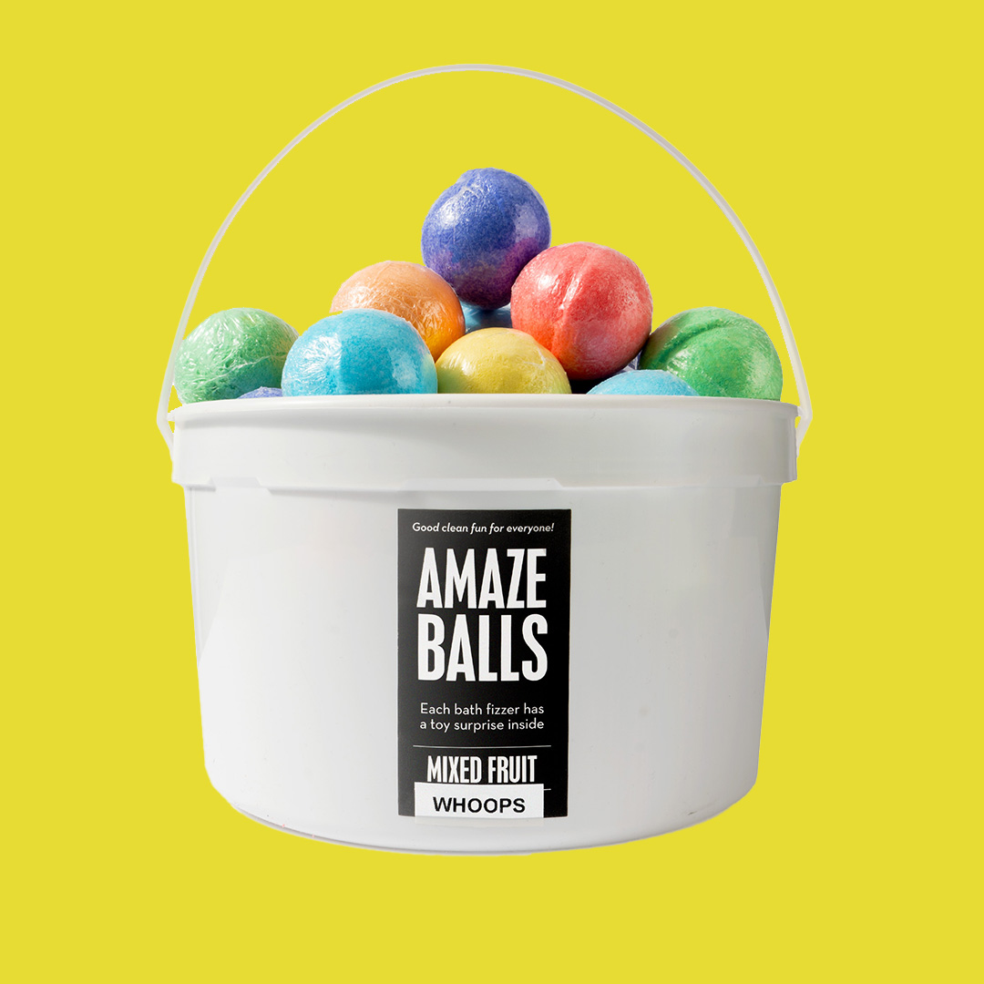 a pile of multi colored bath bombs in a white bucket on a yellow background