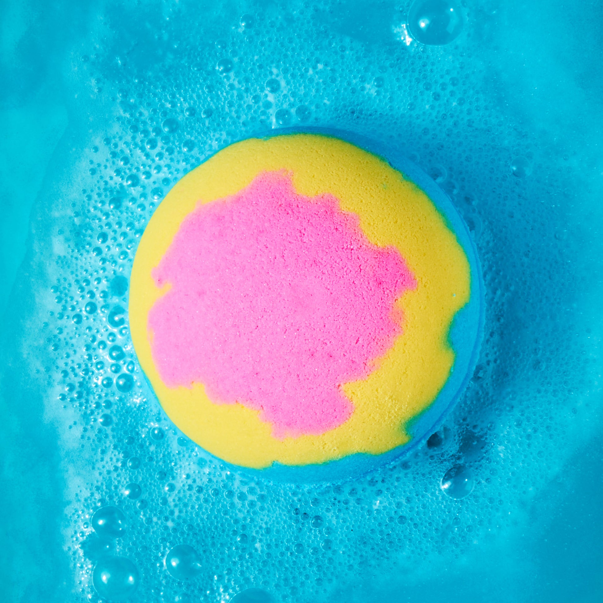Layered pink, yellow, and blue bath bomb fizzing in water