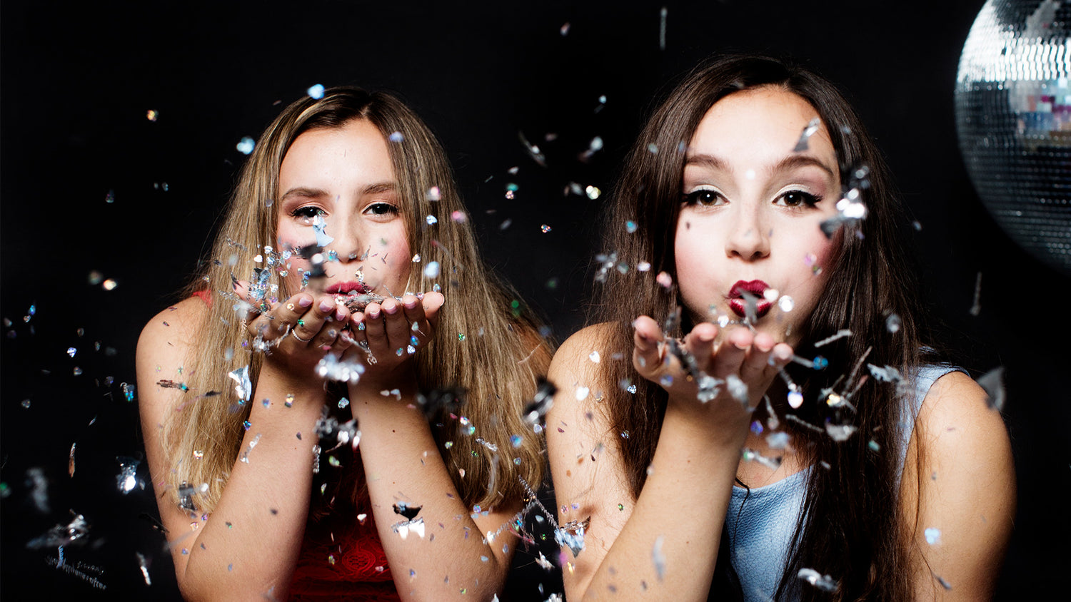two sisters blowing confetti with black background