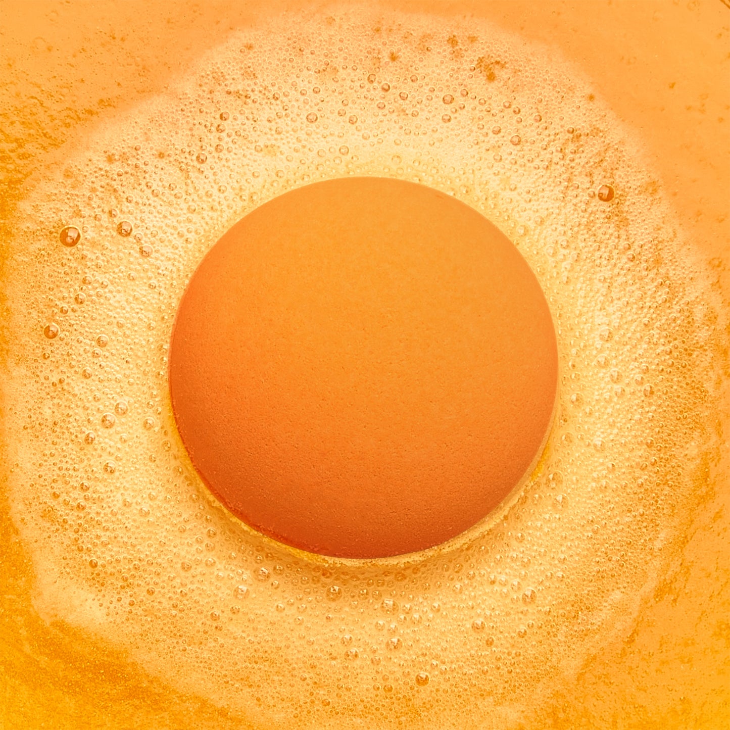 an orange fizzing bath bomb in orange bubbly water