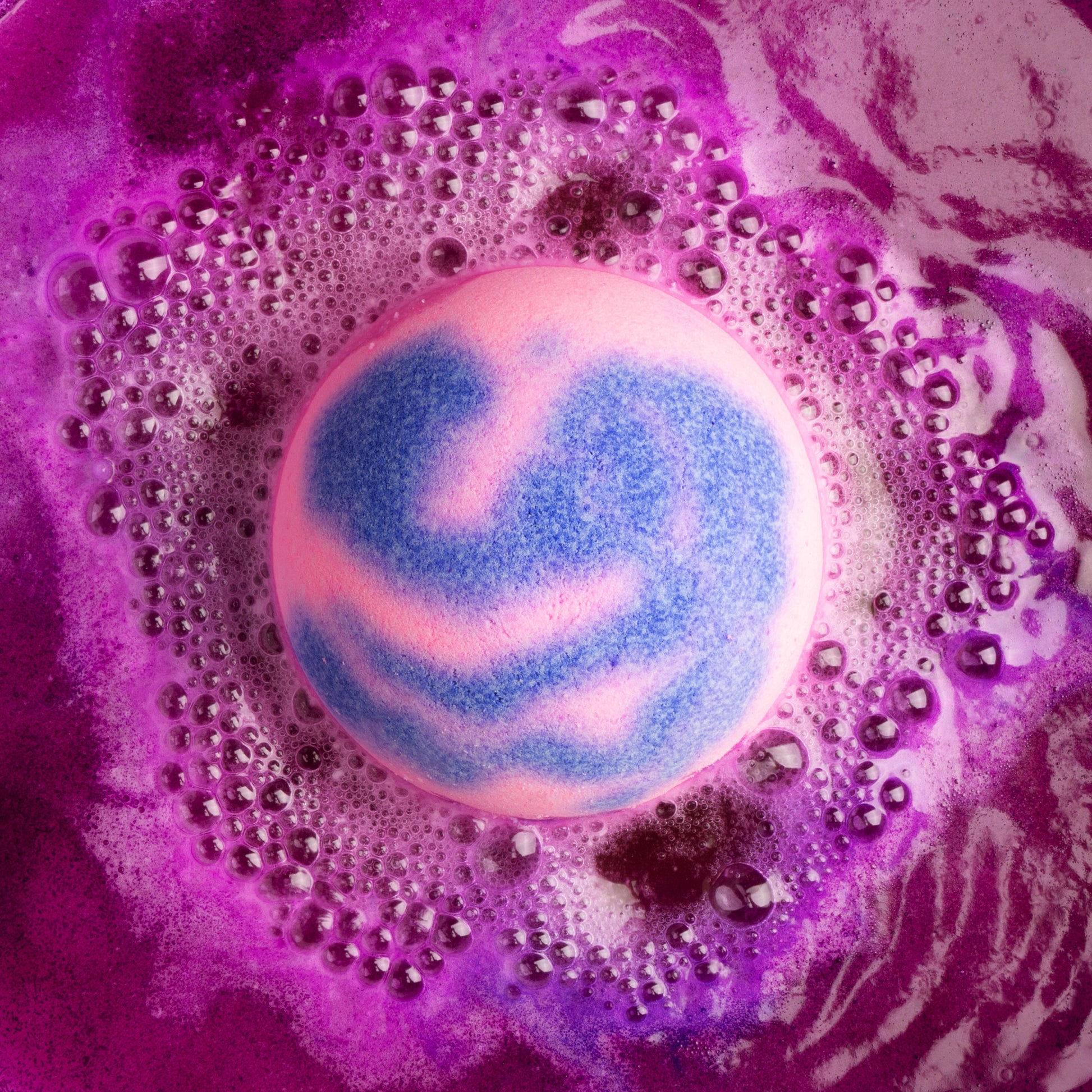 Pink and purple swirl bath bomb fizzing in water