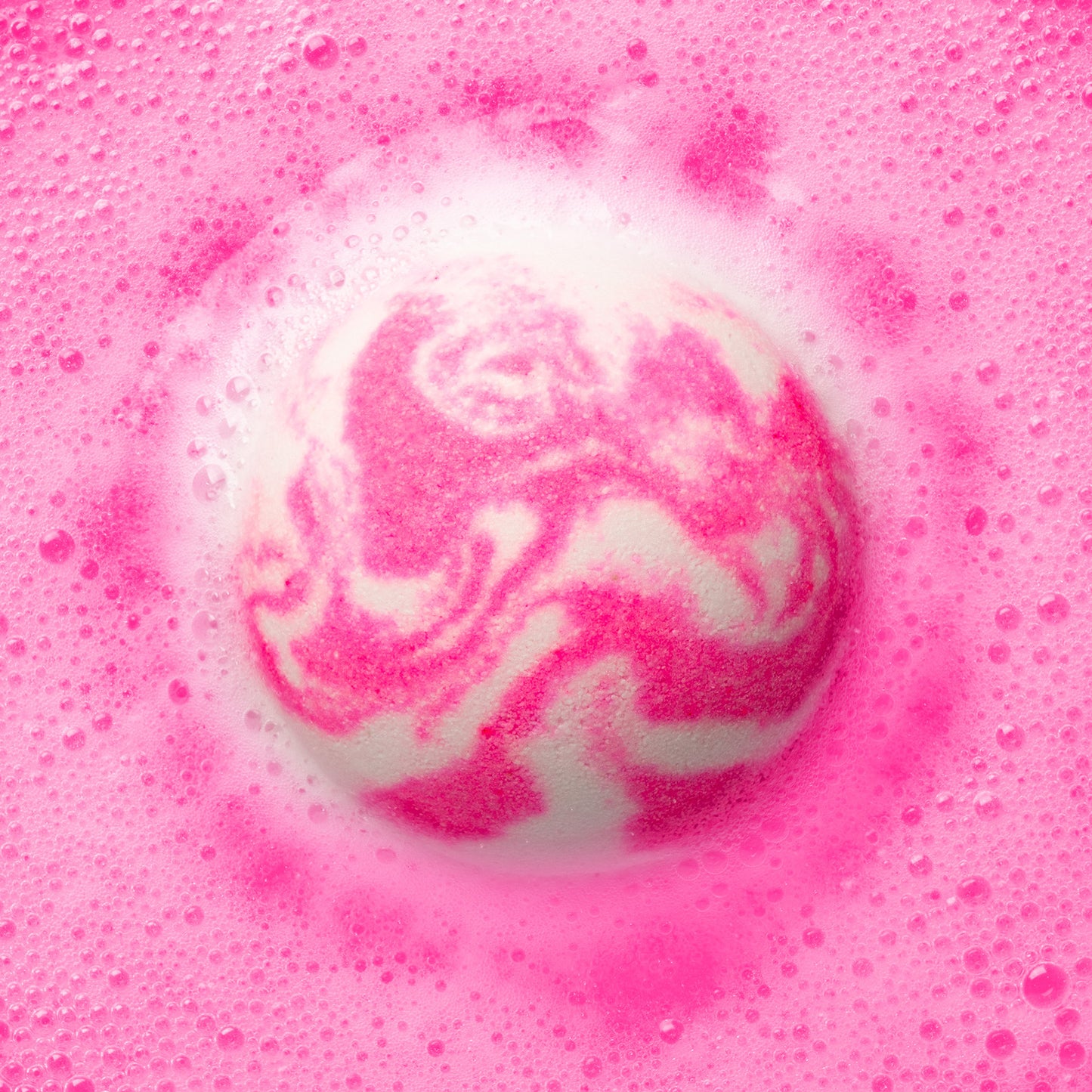 a pink and white bath bomb fizzing in pink water