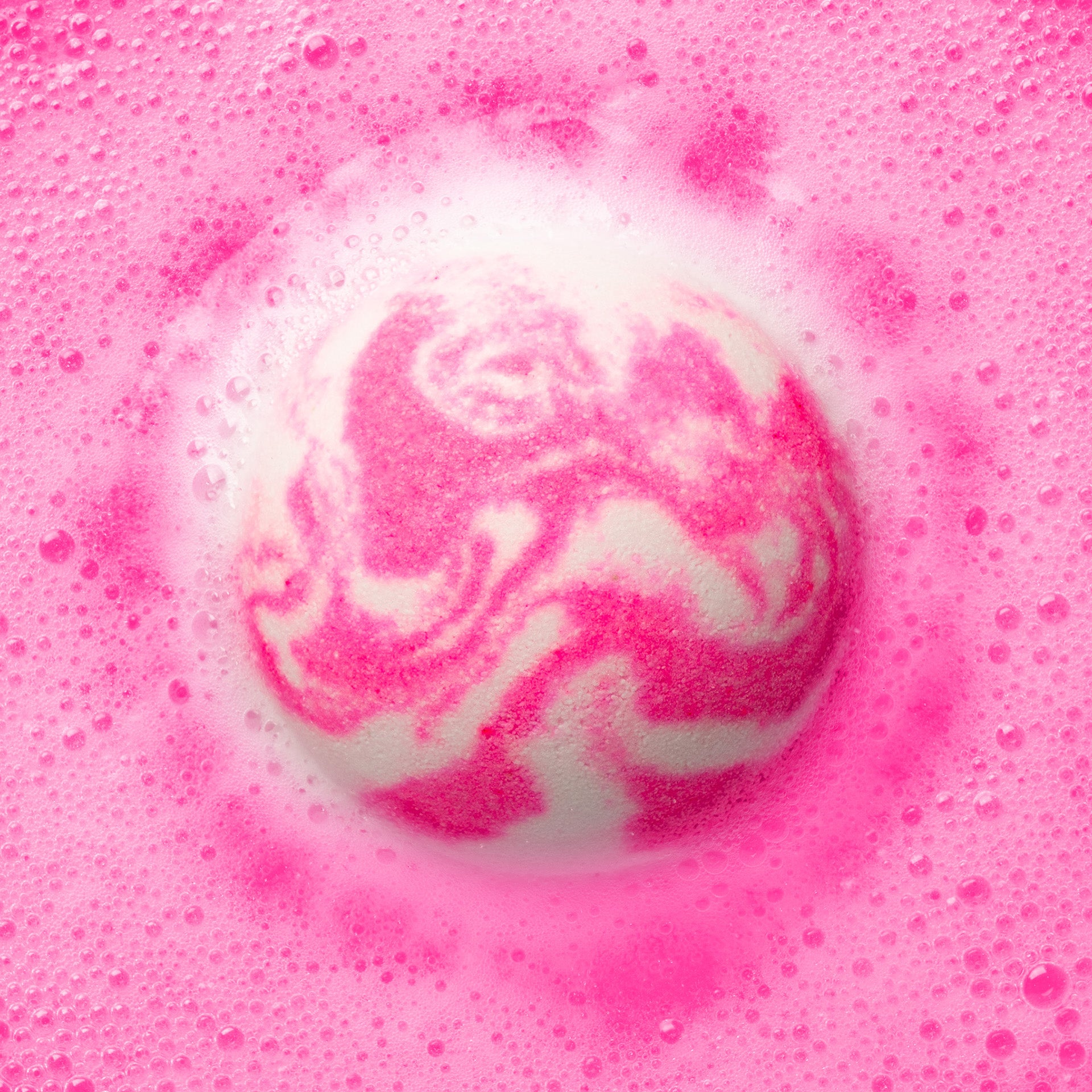a pink and white bath bomb fizzing in pink water