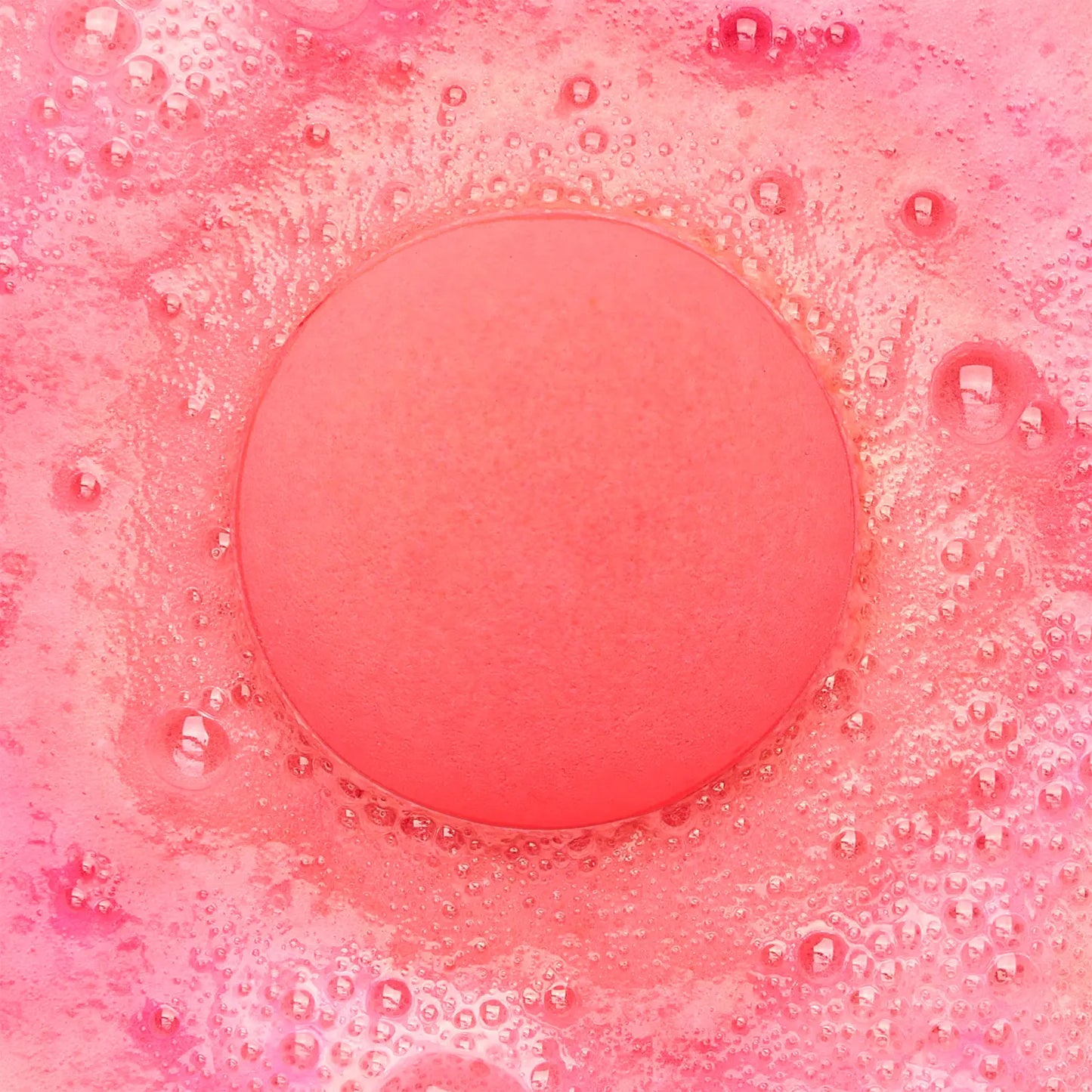 a pink fizzing bath bomb in pink water