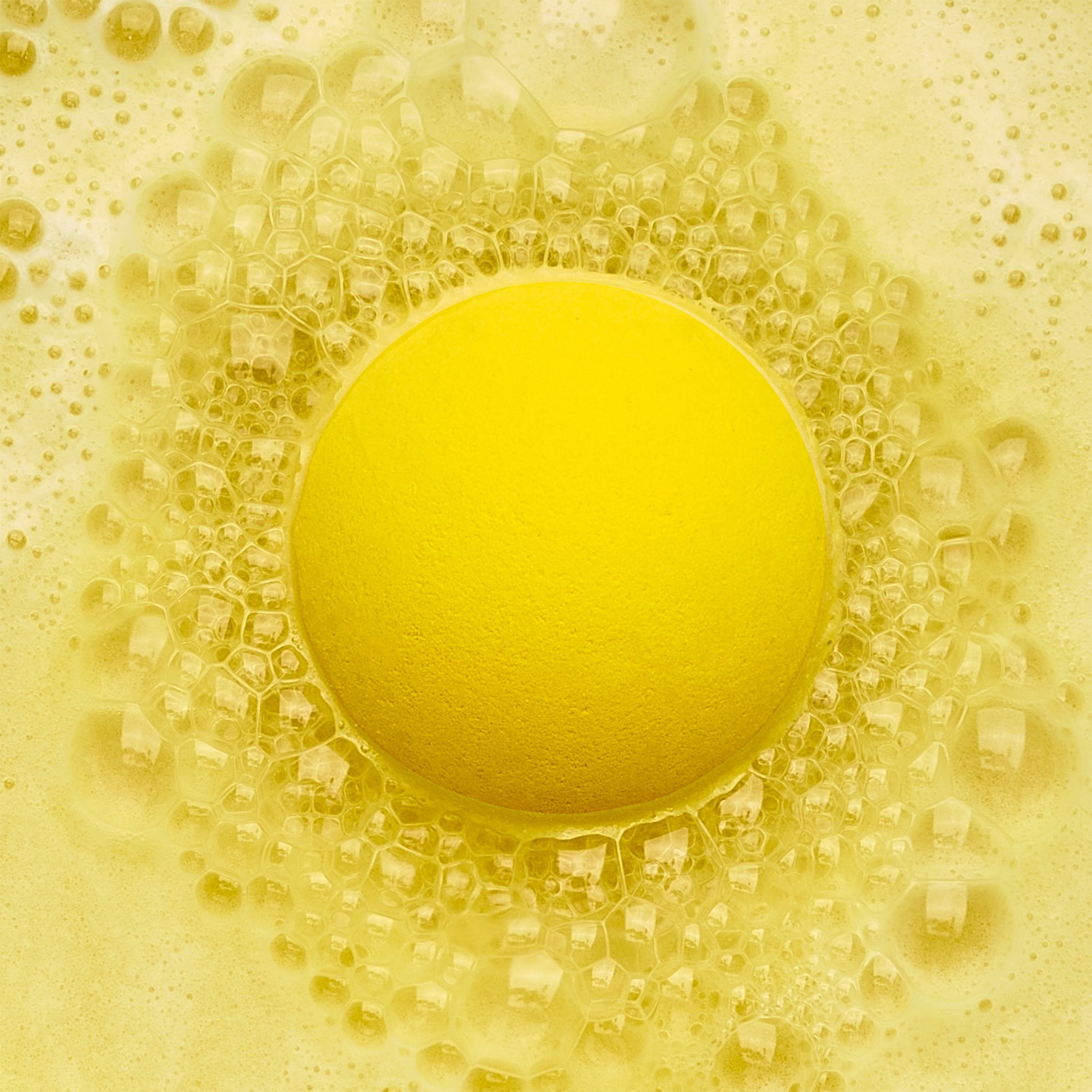 Yellow fizzing bath bomb in yellow bubbly water