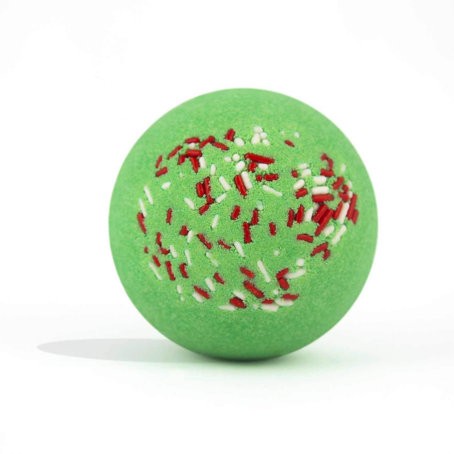 Green with red and white sprinkles, round bath bomb out of packaging on white background.
