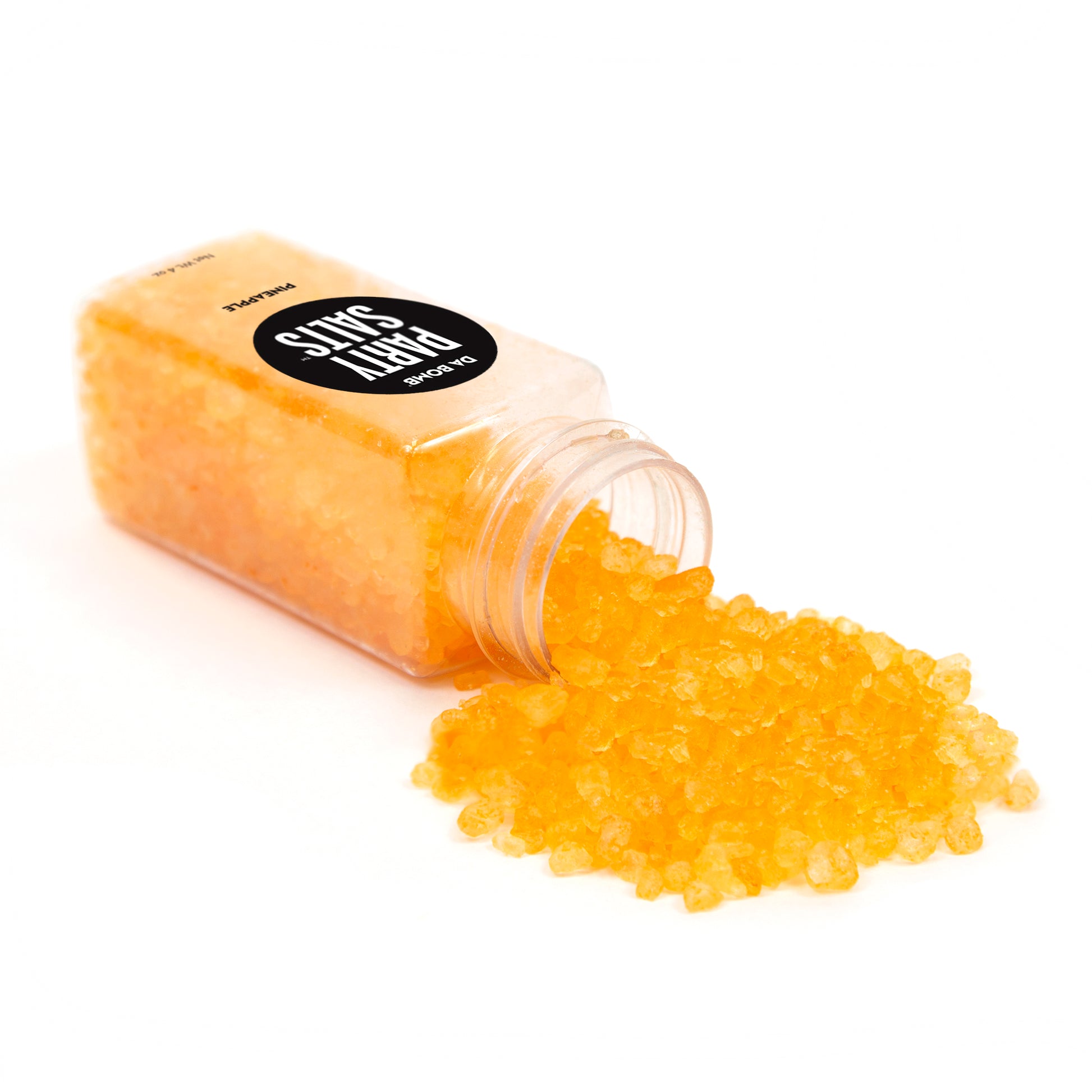 Clear mini jar with orange bath salts spilling out of it onto a white background.