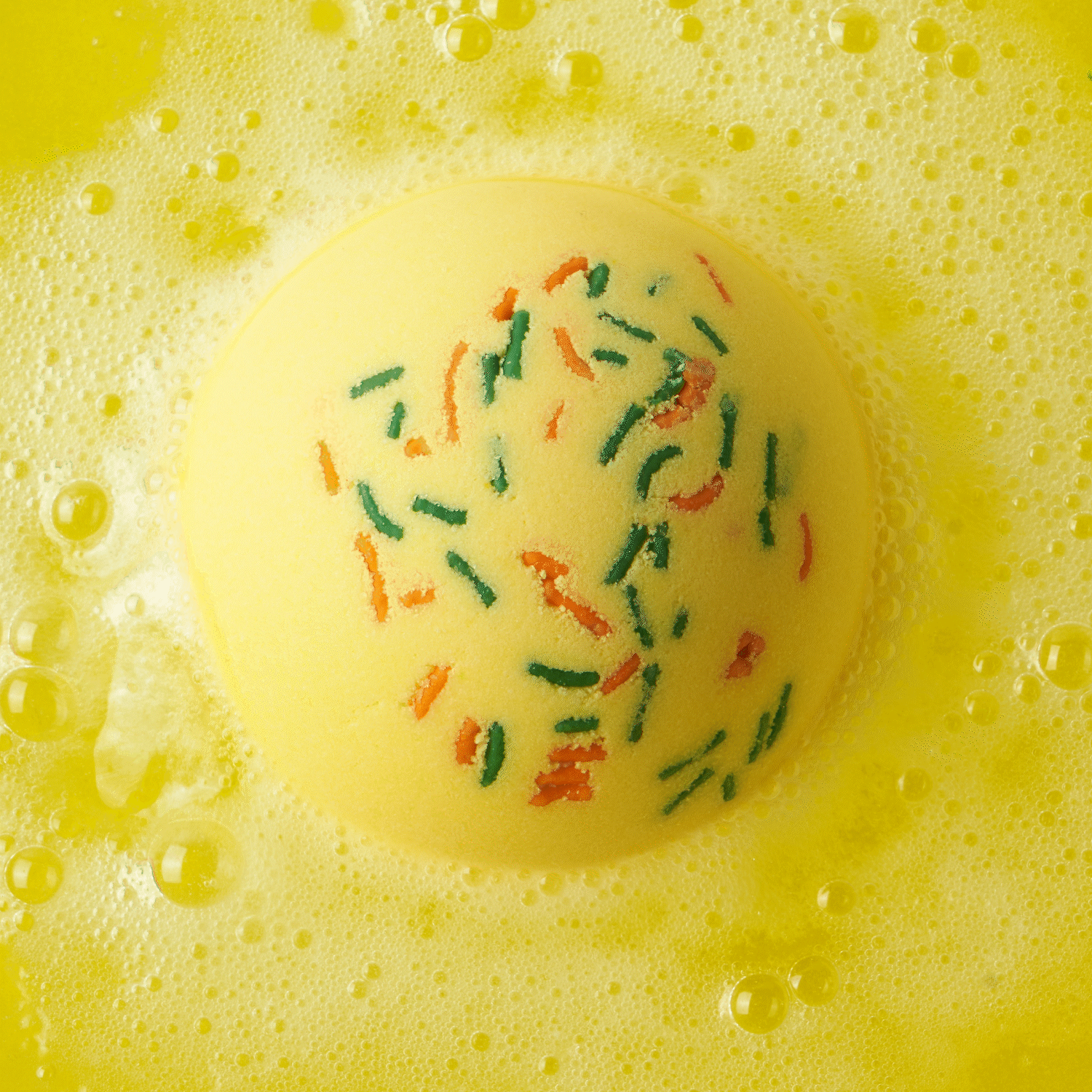 Animated GIF of a fizzing yellow bath with green and orange sprinkles, dissolving in water