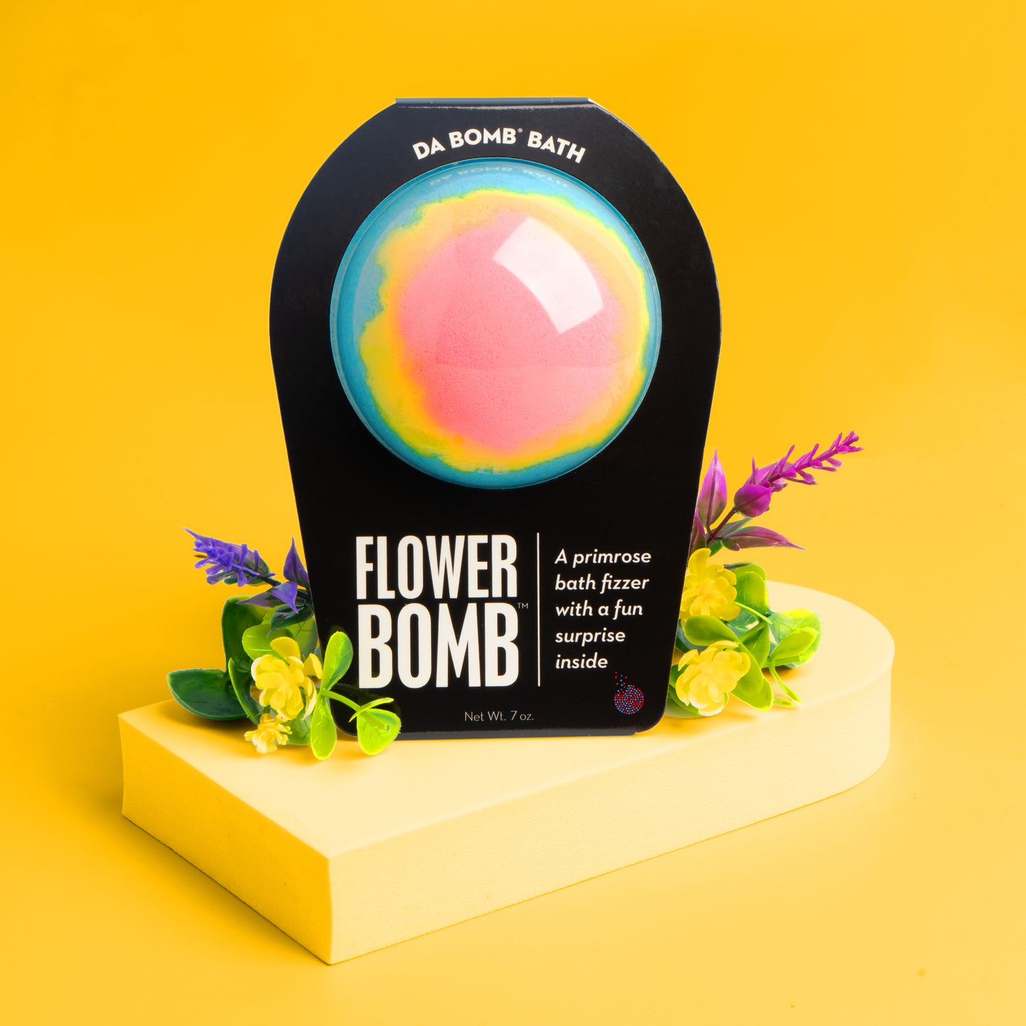 multicolored bath bomb on yellow riser with flowers on both sides