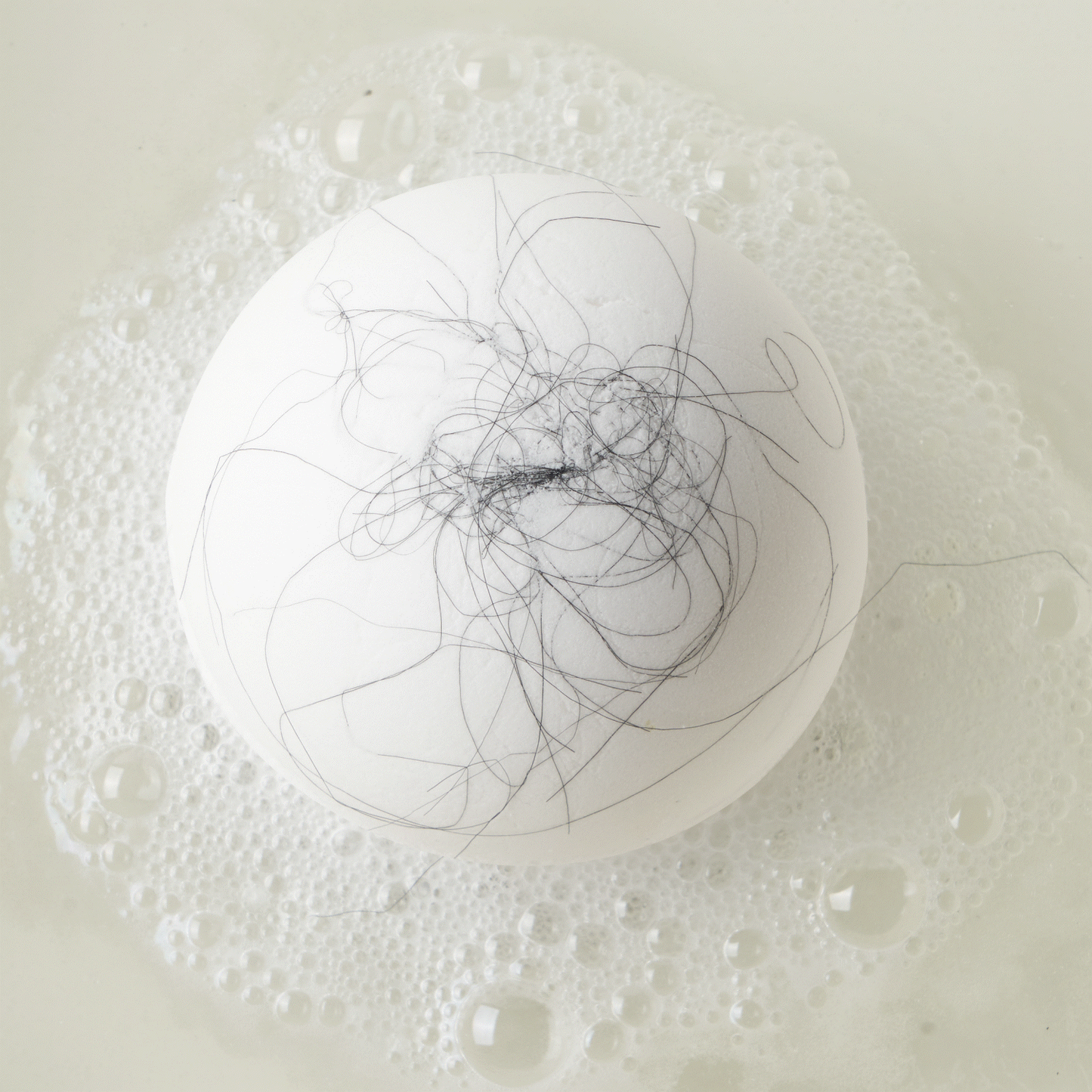 Animated GIF of a white bath bomb fizzing in water with black strands of hair 