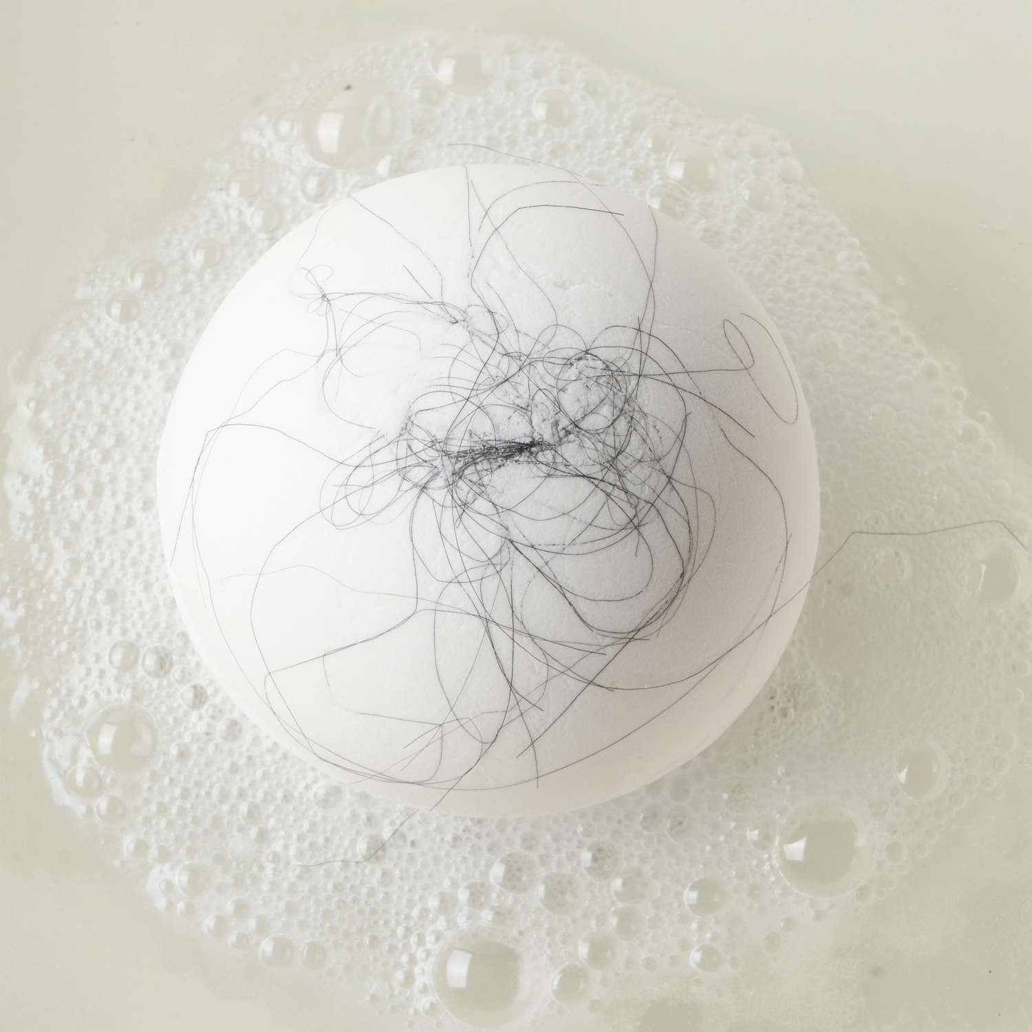 Animated GIF of a white bath bomb fizzing in water with black strands of hair 