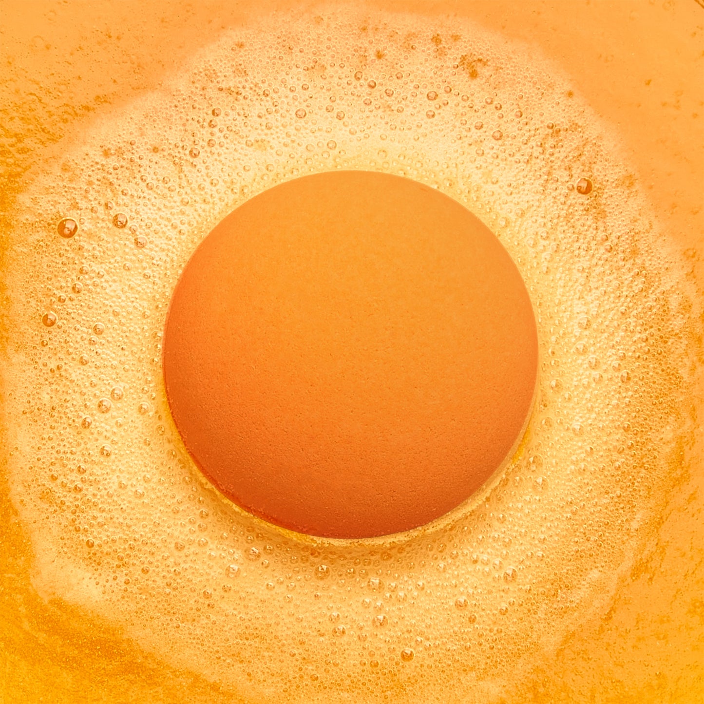an orange fizzing bath bomb in orange bubbly water