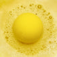 a yellow fizzing bath bomb in yellow bubbly water