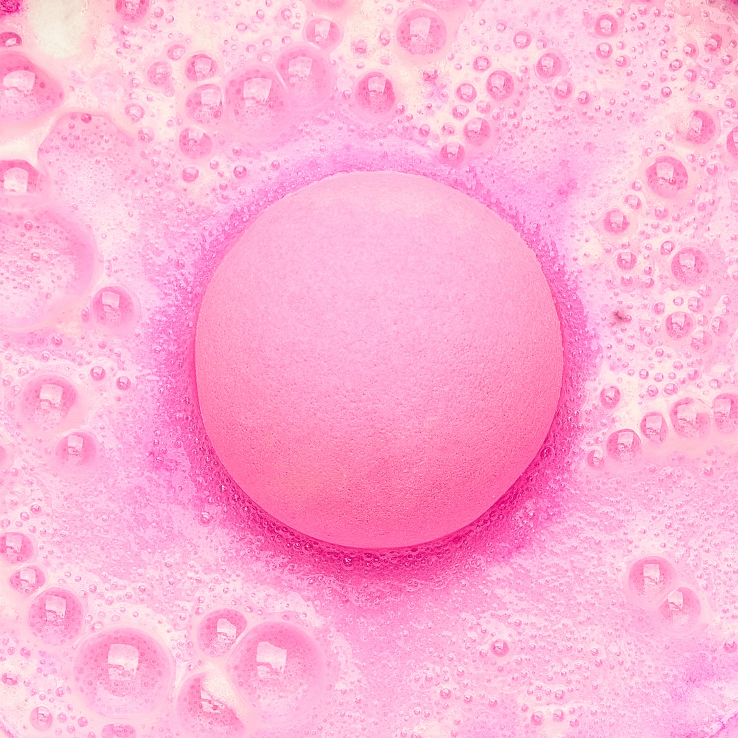 a pink fizzing bath bomb in pink water