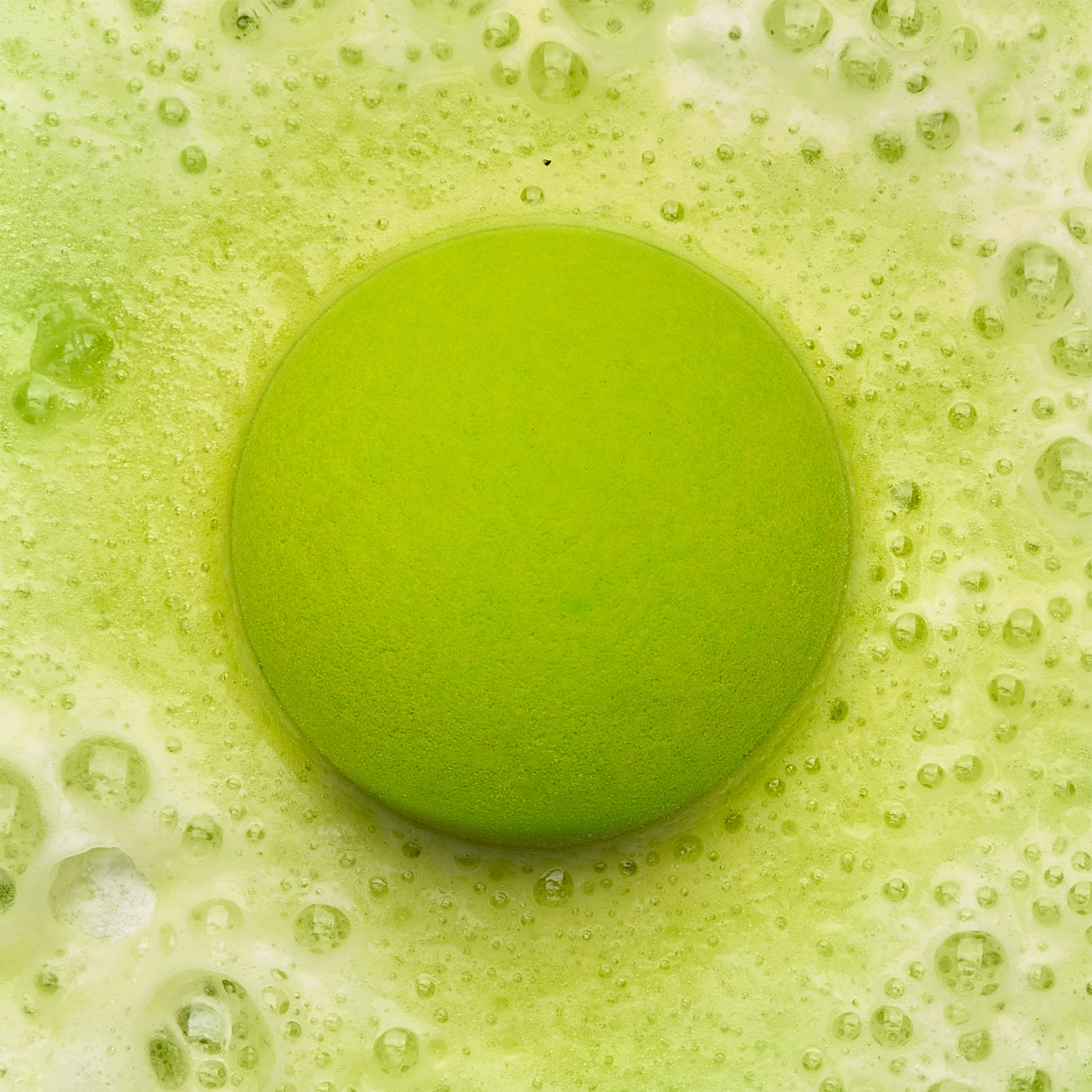 a green fizzing bath bomb in green water