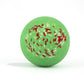 Green with red and white sprinkles, round bath bomb out of packaging on white background.