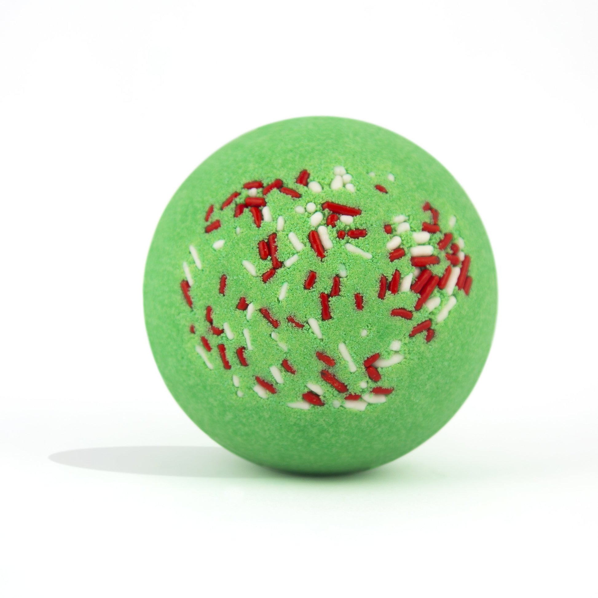 Green with red and white sprinkles, round bath bomb out of packaging on white background.